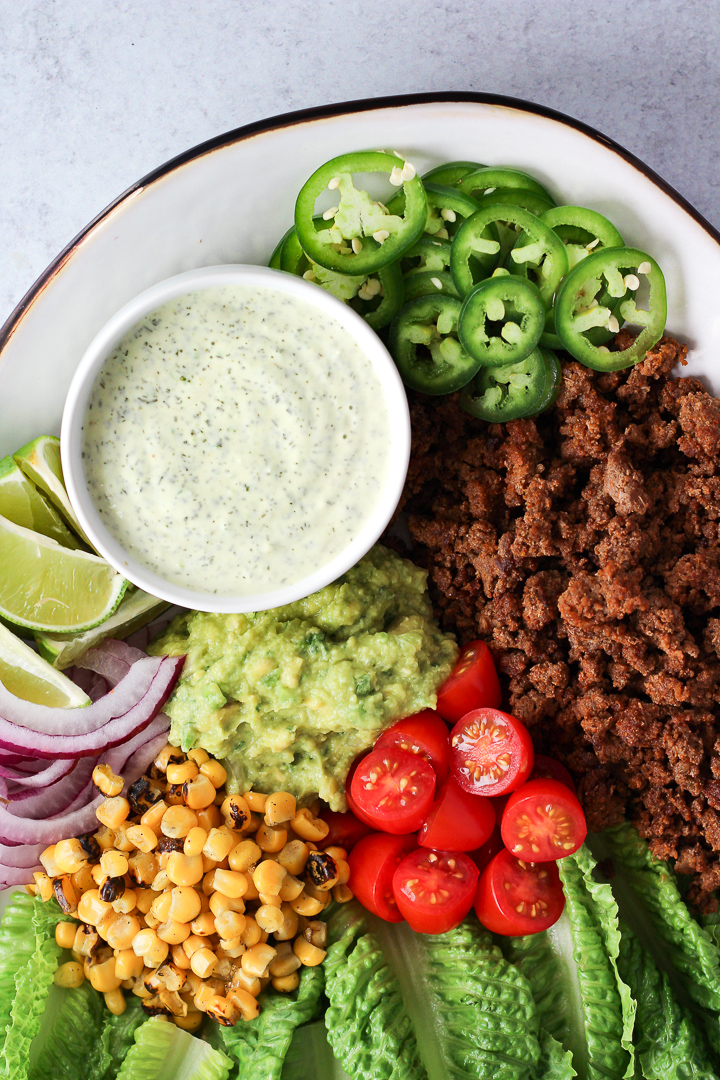 Taco salad platter with lettuce, ground beef, sliced jalapenos and small bowl of ranch dressing