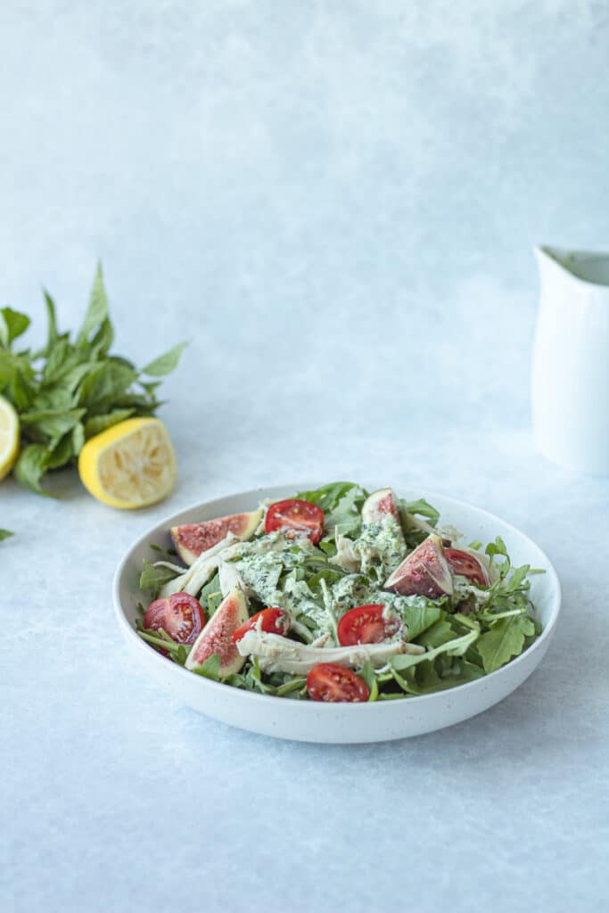 green goddess dressing on salad with herbs behind