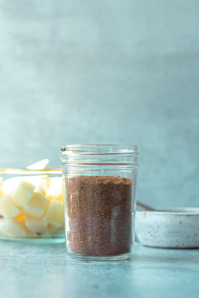 spice mix in jar with bowl of potatoes behind