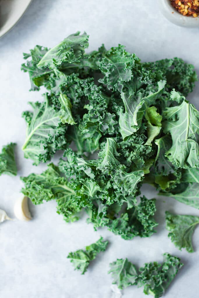 pile of raw kale leaves with garlic cloves