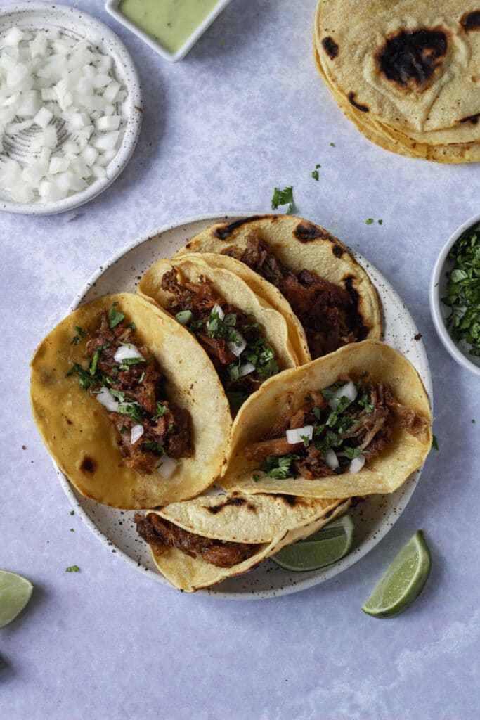 Crispy carnitas tacos with toppings around plate