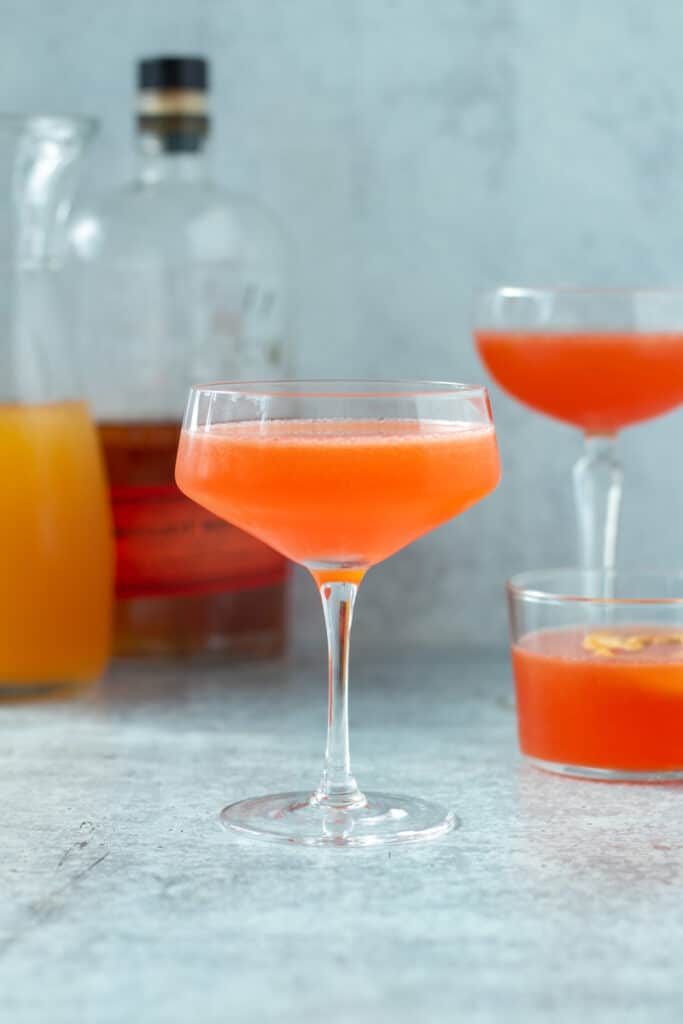 apple cider bourbon cocktail in coup glass with drinks behind 