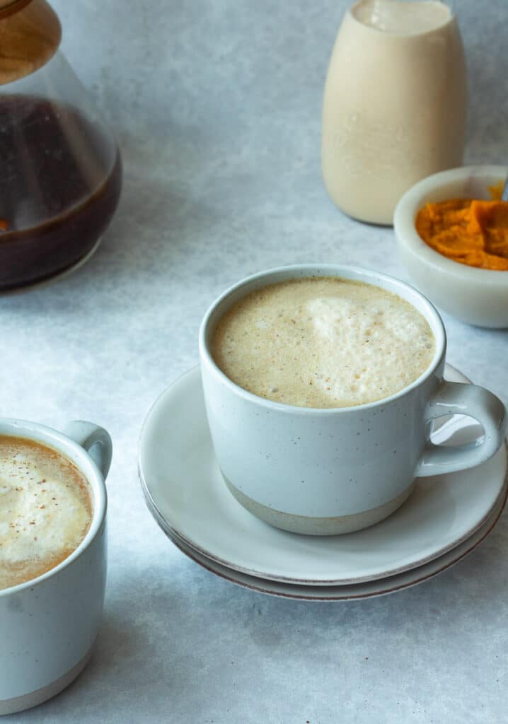 2 mugs of pumpkin cream cafe au lait with pumpkin and coffee in back