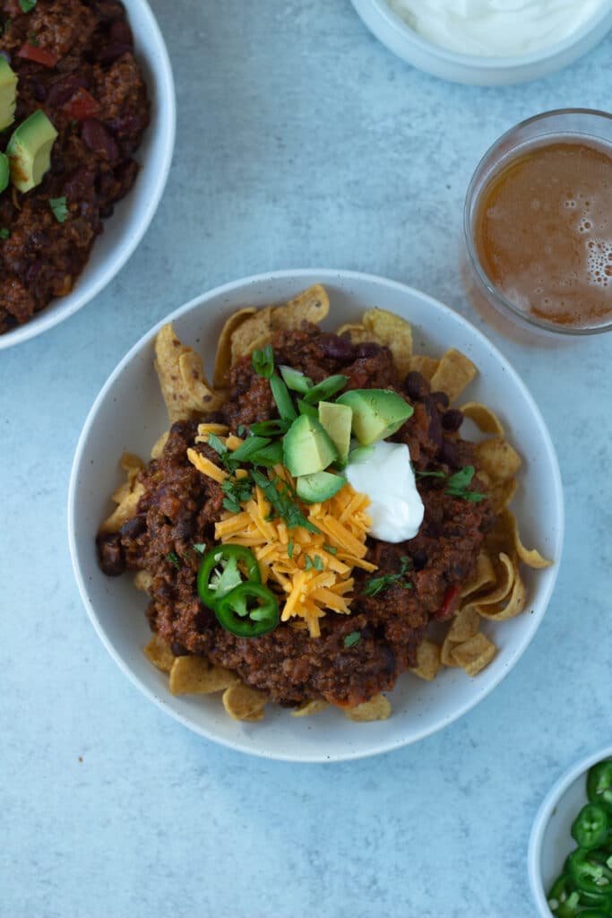 Finished bowl of thick chili with toppings and glass of beer. 