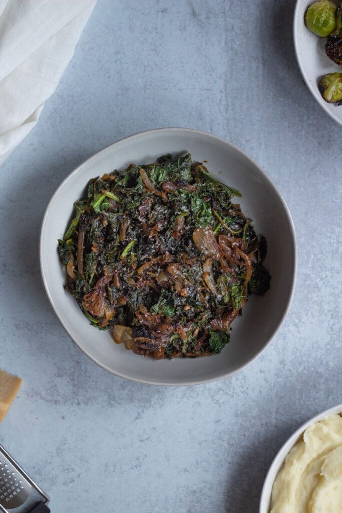 bowl of kale and caramelized onions with bowl of brussels sprouts on the side