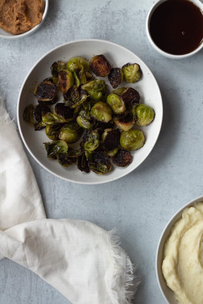 bowl of brussels sprouts next to plate of mashed potatoes and bowl of maple syrup
