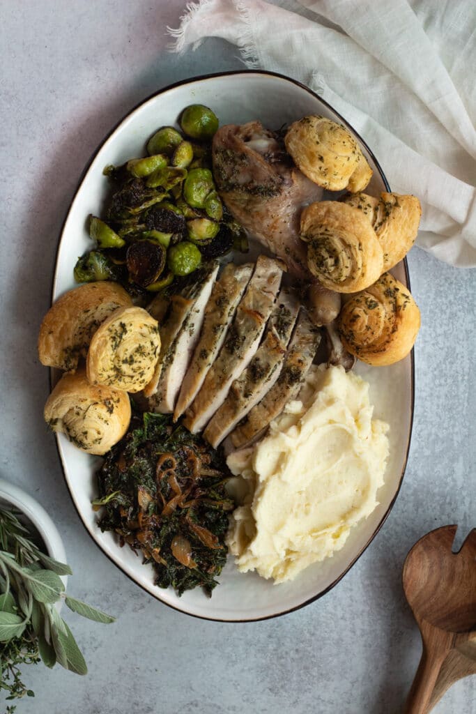 Platter of thanksgiving meal with turkey, brussels sprouts, rolls, mashed potatoes and kale