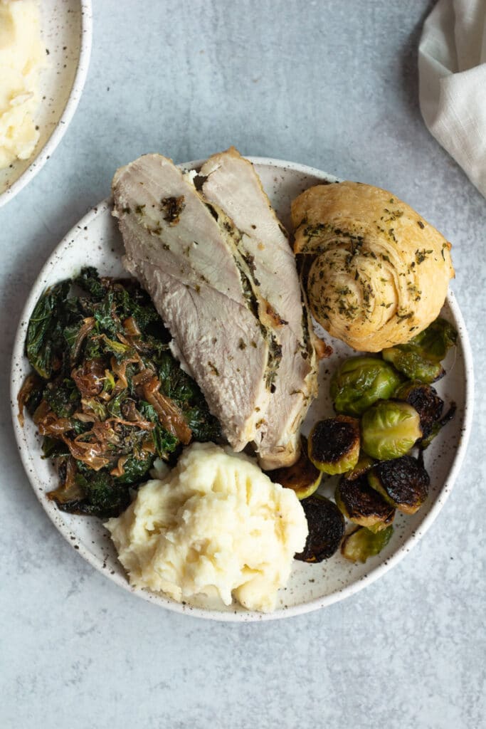 round plate of thanksgiving food with turkey, rolls, kale and mashed potatoes