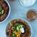 two bowls of chili with toppings and glass of beer