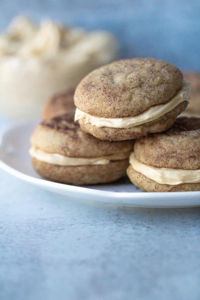 three chai snickerdoodle sandwich cookies on plate with bowl of filling behind