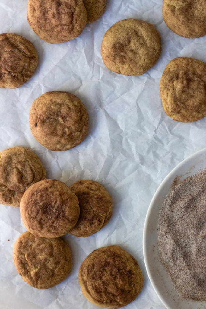 chai snickerdoodle cookies on parchment paper with plate of chai sugar mix in corner