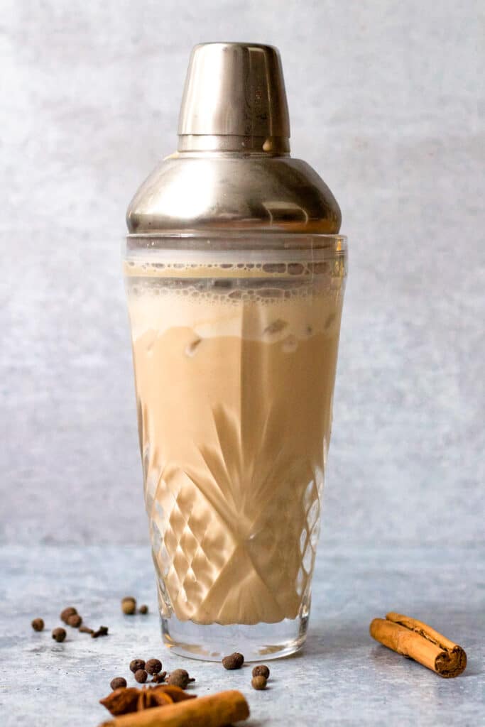 white russian in glass shaker with cinnamon sticks, star anise and spices surrounding glass