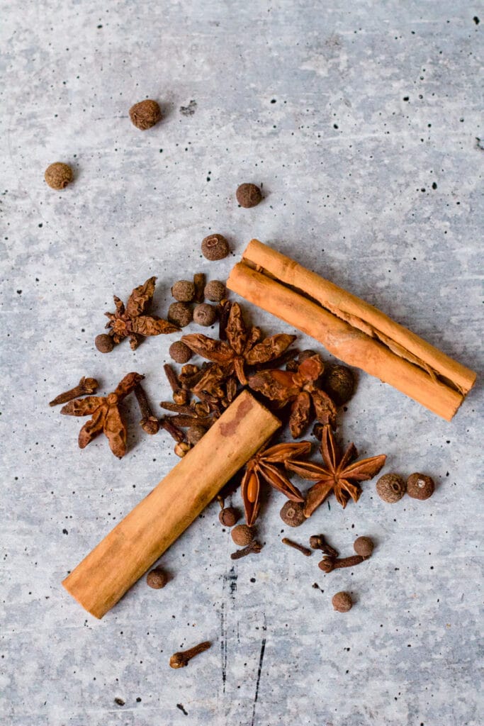 pile of cinnamon sticks, allspice berries and cloves on background