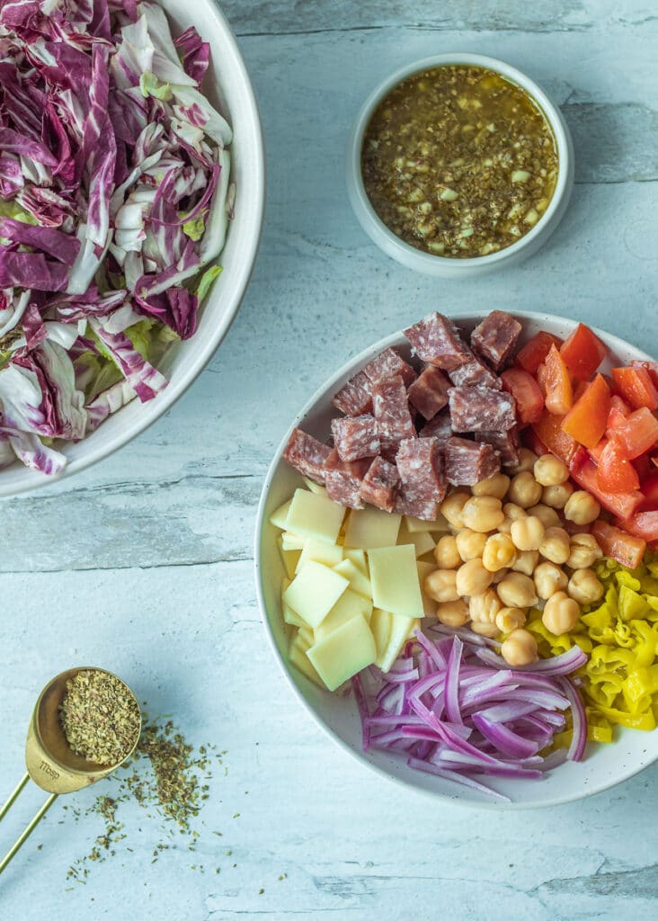 components of italian chopped salad with lettuce, onion, peppers, salami, provolone cheese and garlic dressing