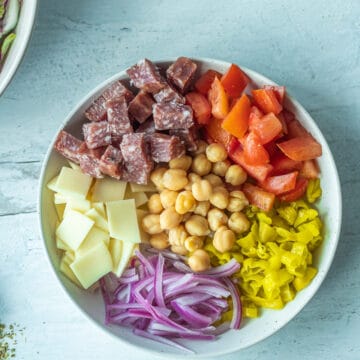 salami, peppers, onions, cheese and tomatoes in bowl for italian chopped salad