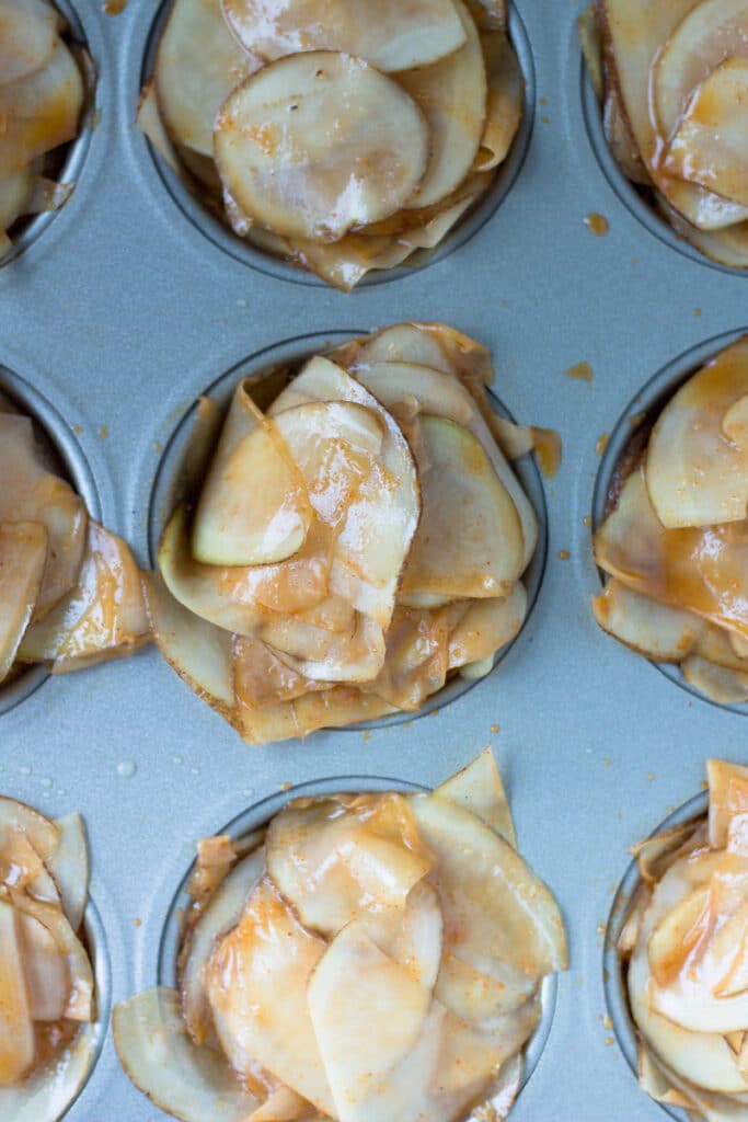 raw potatoes stacked in muffin tin before roasting