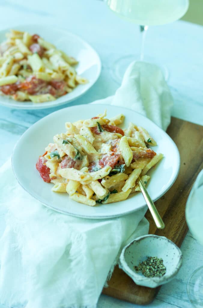 Plate of tomato and feta pasta with gold fork and glass of wine