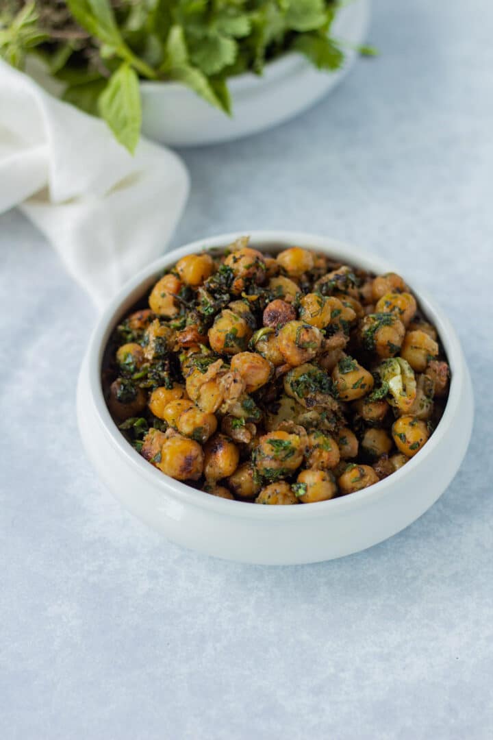 bowl of crispy chickpeas with pile of herbs behind