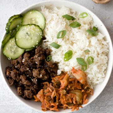 Bowl with ground beef bulgogi, rice, cucumber slices, green onion and sesame seeds