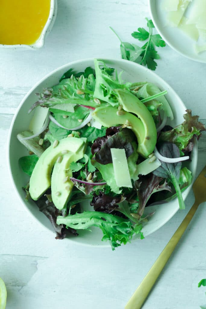 Plate of salad with greens, sliced avocado, sunflower seeds with fork on the side