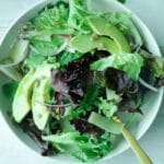 Plate of mixed salad with greens, avocado, sunflower seeds, red onion slices and dressing