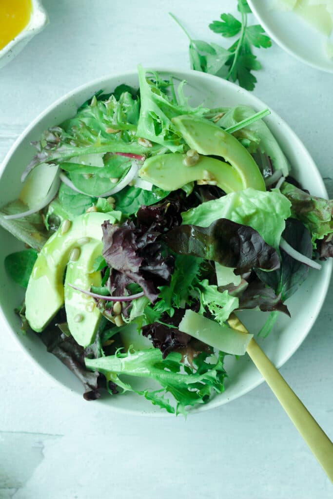 Plate of mixed salad with greens, avocado, sunflower seeds, red onion slices and dressing