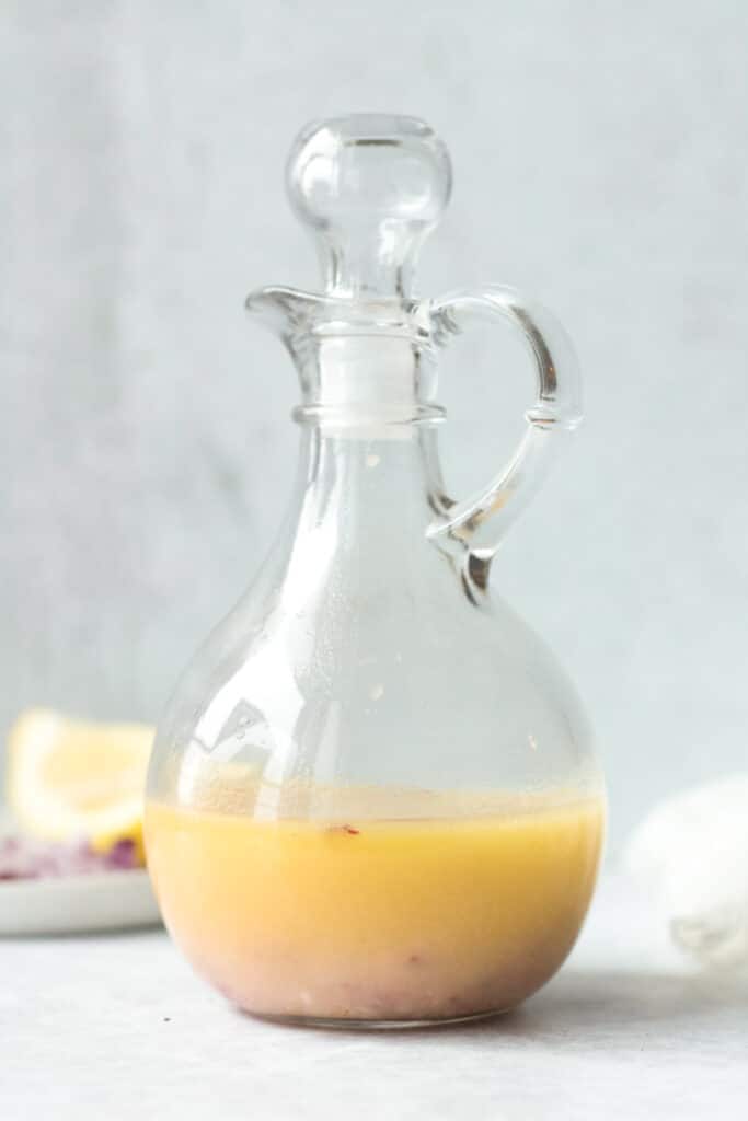 Lemon garlic vinaigrette in glass salad dressing bottle with ingredients on small plate behind
