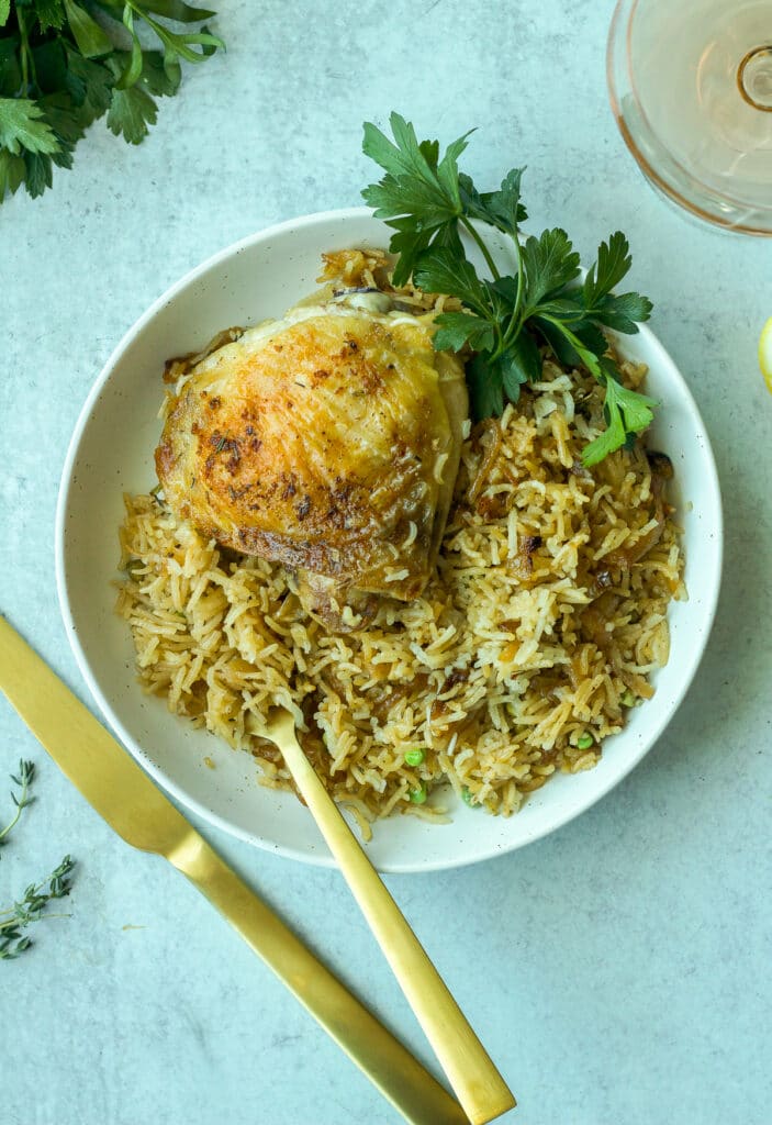 Plate with chicken thigh and rice, gold silverware and a glass of wine