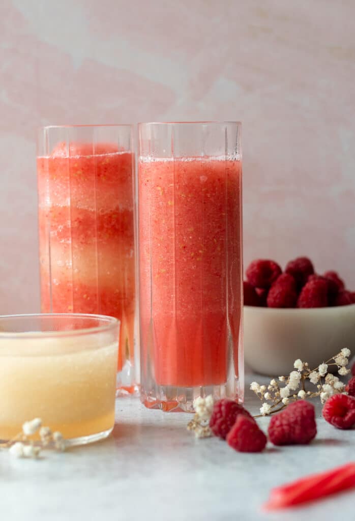 glasses of raspberry limoncello frosé with a small glass of limoncello, a striped straw and fresh raspberries