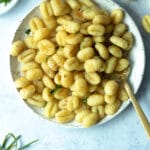 roasted gnocchi with lemon garlic brown butter on plate surrounded by chives, a small bowl of flaky salt and garlic cloves