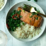 Salmon and rice on plate with herb chili mix with cilantro leaves around plate