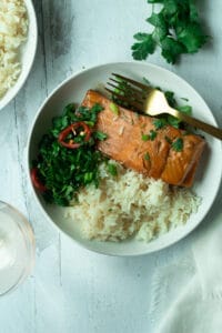 Salmon and rice on plate with herb chili mix with cilantro leaves around plate