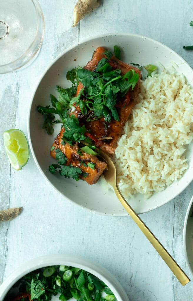 Fork taking bite out of salmon filet on plate with rice