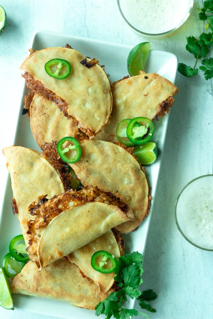 Platter of baked chicken tacos with lime wedges and cilantro on top and glasses of beer on side