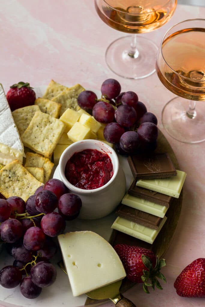 close up shot of cheese board with red grapes, chocolate bars, cheese knife and strawberries