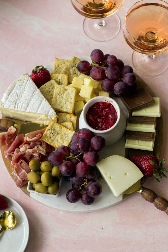 cheese board with cheese, fruits, snacks and two glasses of rose wine