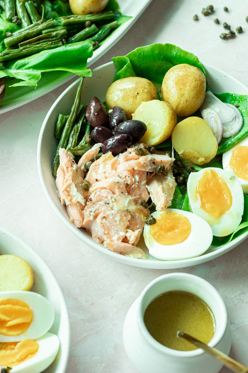 bowl of salmon niçoise salad with small jar of dressing on side