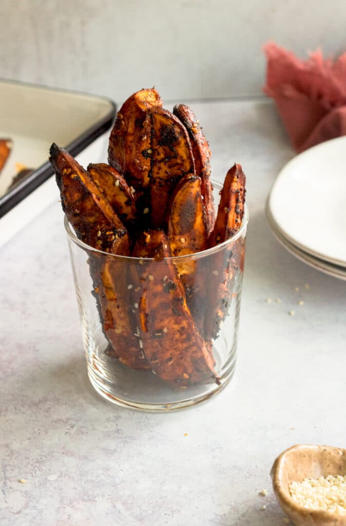 gochujang sweet potatoes in glass with small bowl of sesame seeds