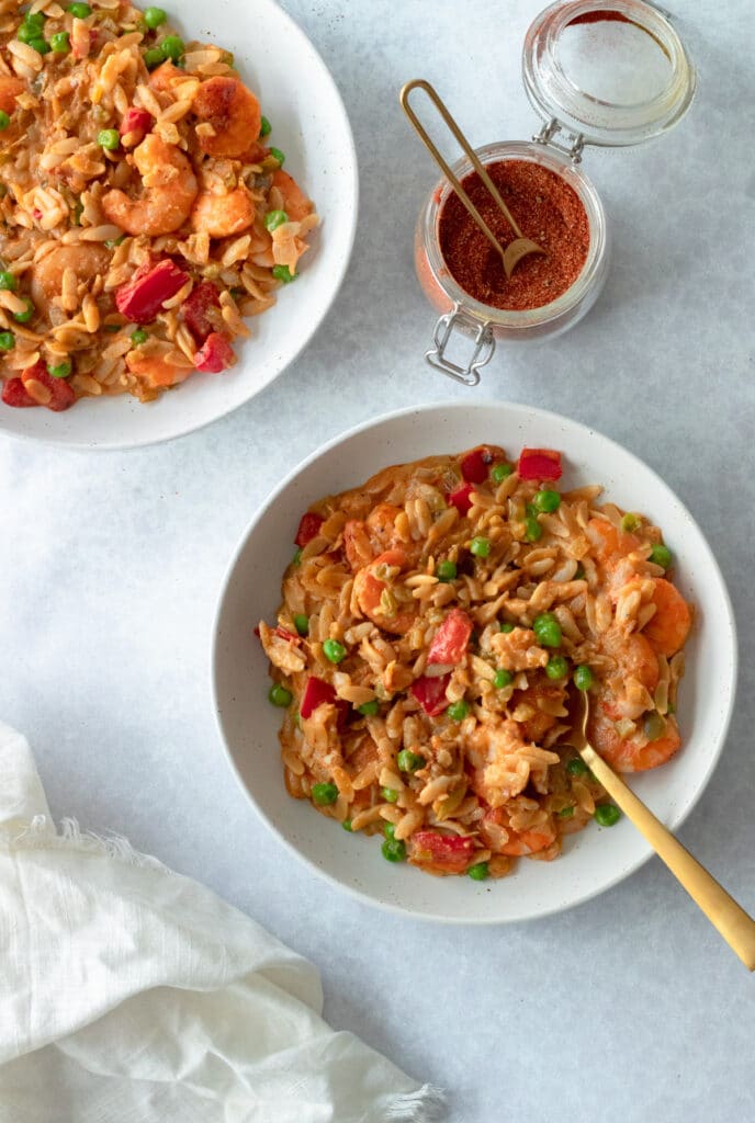 bowls of orzo with shrimp with small jar of cajun seasoning on table