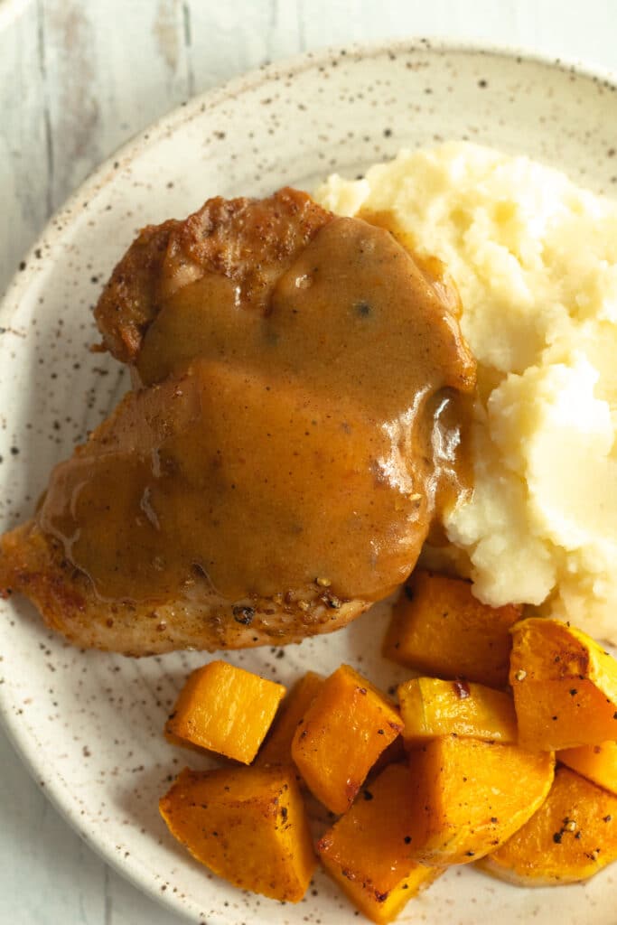 close up of plate with apple cider chicken covered in sauce next to squash and potatoes