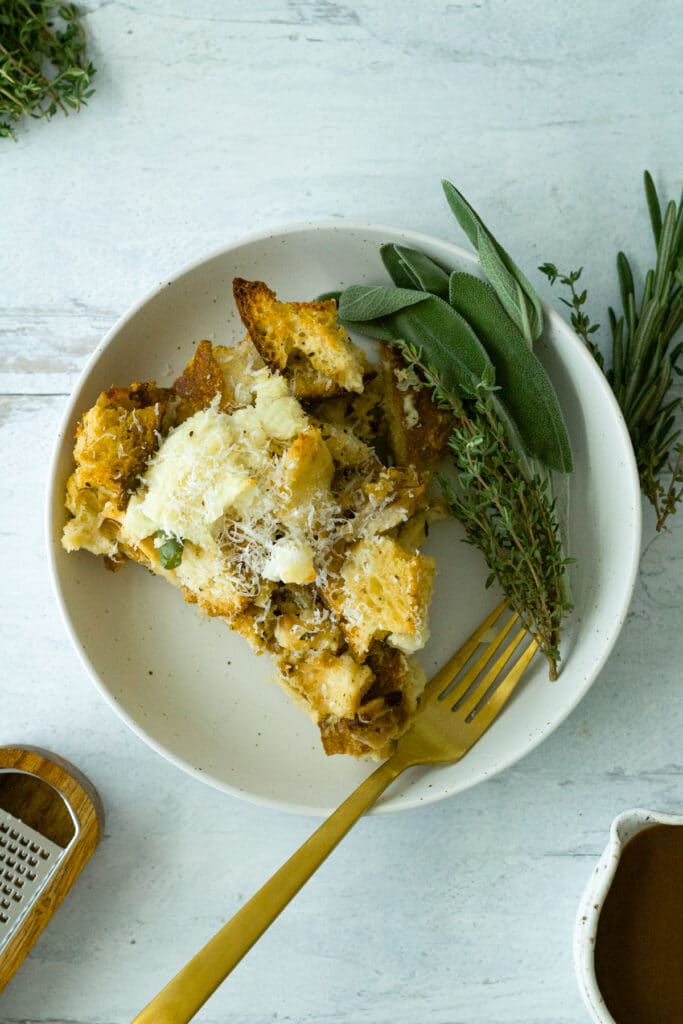 serving of strata on plate with gold fork, herb garnish and grated parmesan cheese