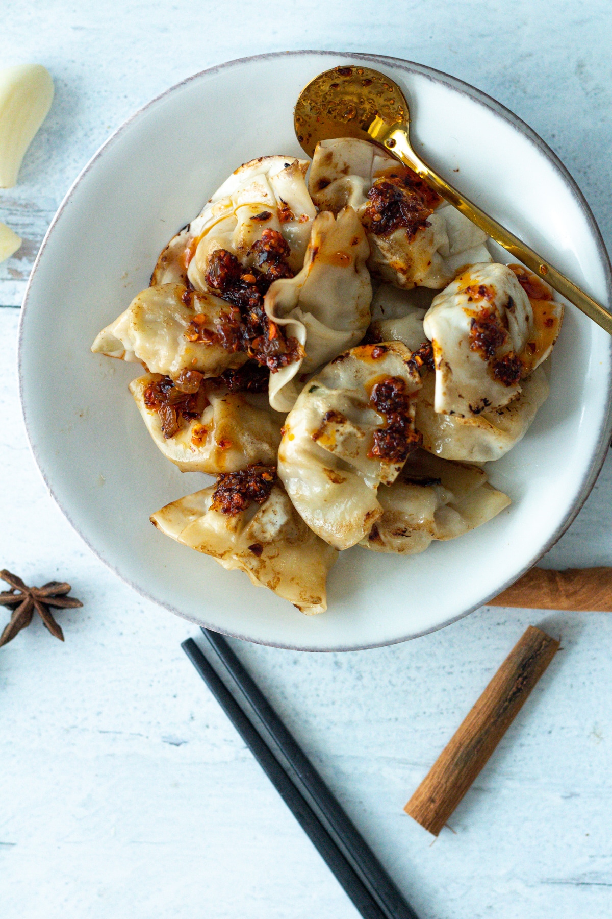 garlic chili oil on dumplings on small plate with chopsticks.