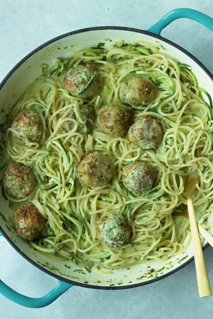 Pot of creamy pesto pasta and chicken meatballs with gold silverware