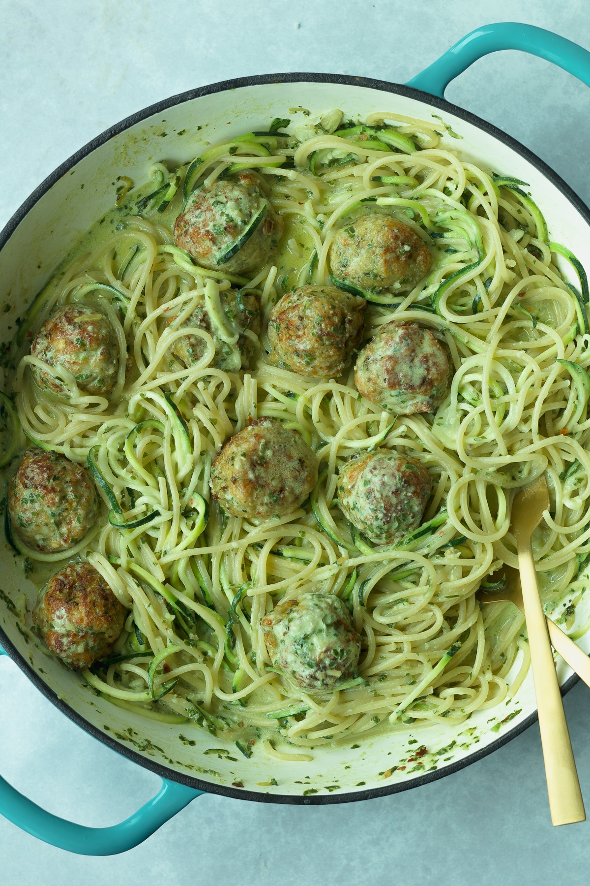 Pot of basil pesto cream sauce and chicken meatballs with pasta.