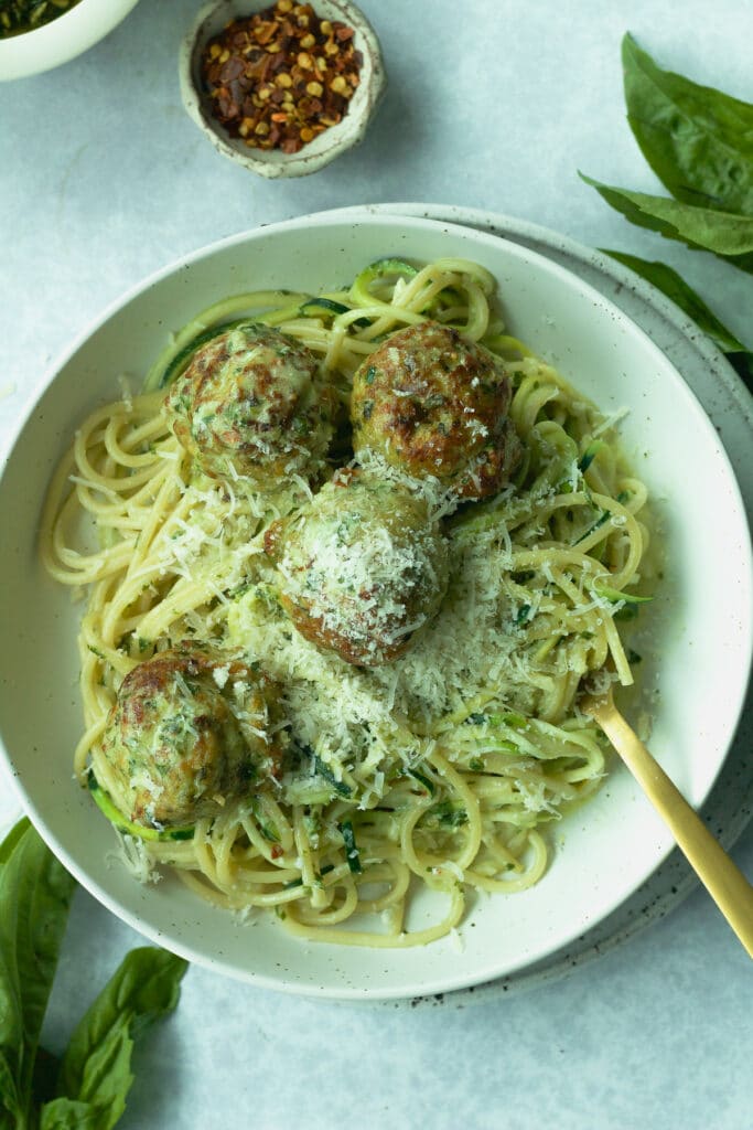 Bowl pasta with chicken meatballs with grated parmesan cheese on top and fork in bowl.