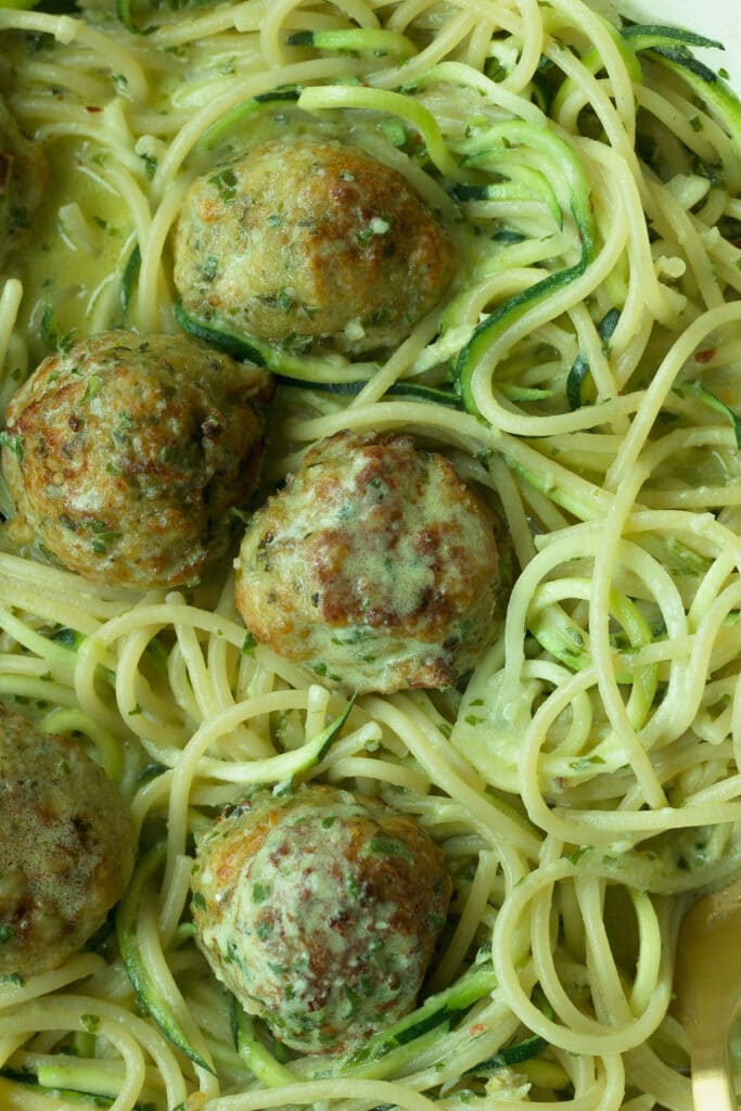 closeup of pesto chicken meatballs with basil pesto cream sauce pasta.