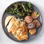 plate with one pan chicken breast and crispy potatoes and kale.