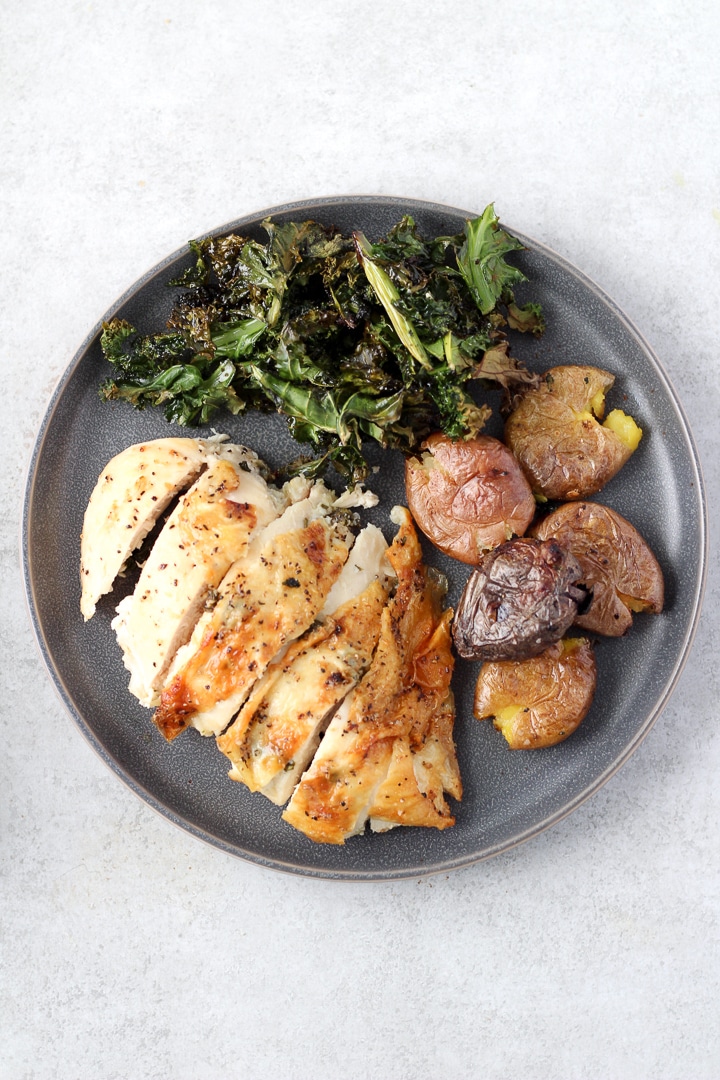 plate with one pan chicken breast and crispy potatoes and kale.