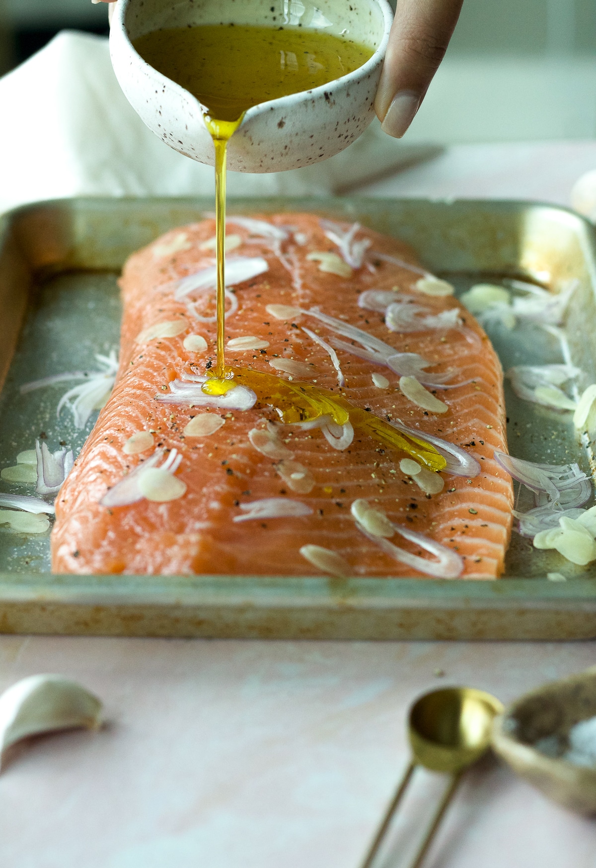 Salmon on baking sheet with shallots and garlic and hand pouring olive oil.
