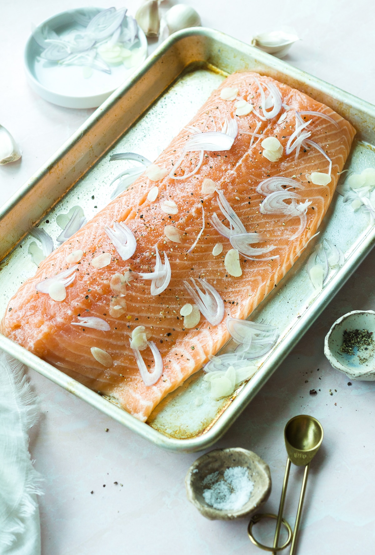 Raw salmon filet on baking sheet with thinly sliced shallot and garlic on top.